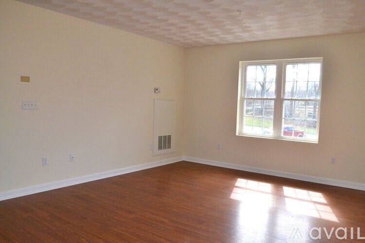 A room with wooden floors and a window with a view of a parking lot.