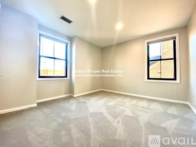 A room with a carpeted floor and two windows.