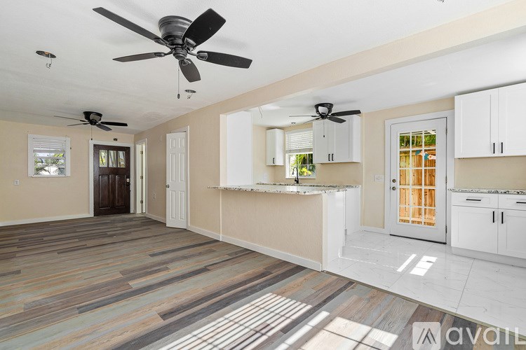 A spacious room with a ceiling fan and a kitchen area with white cabinets.