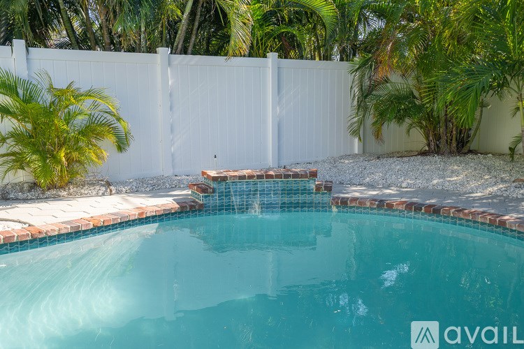 A pool surrounded by a white fence and palm trees.