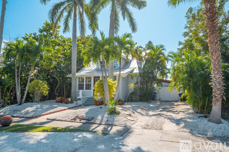 A house with a white fence and a driveway surrounded by trees.