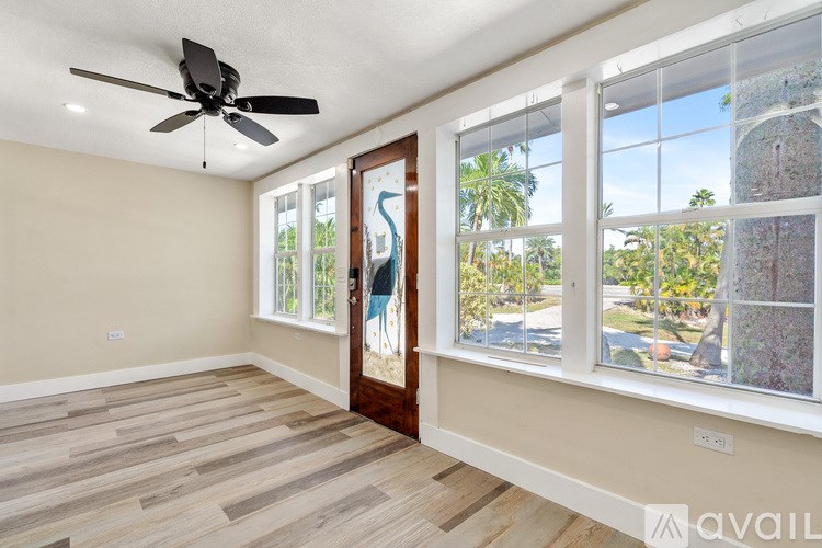 A room with a ceiling fan and a view of a street through the windows.