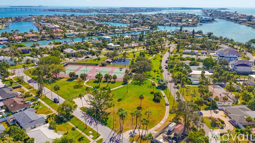 A bird's eye view of a residential area with a sports field and a body of water in the distance.