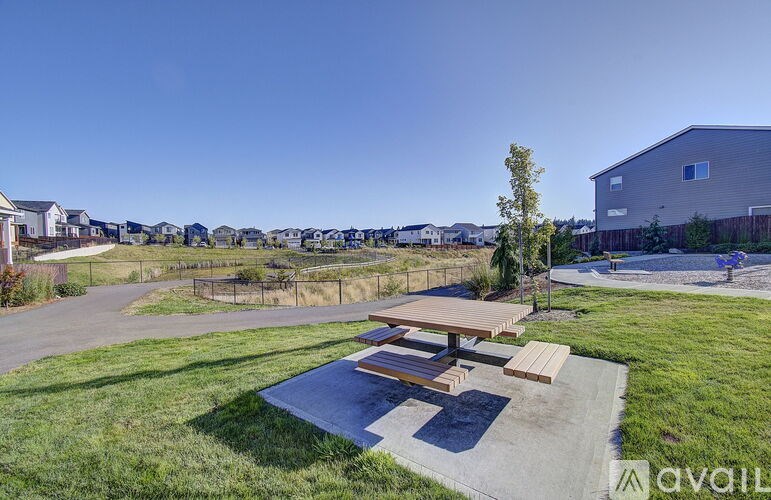 A park area with a picnic table and benches in the foreground and a building in the background.