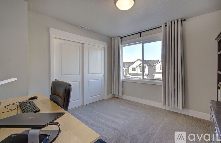 A room with a desk, chair, and a window overlooking a residential area.