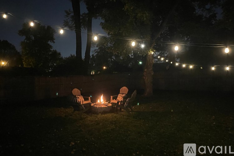 A cozy scene of a campfire surrounded by chairs and trees under the night sky.
