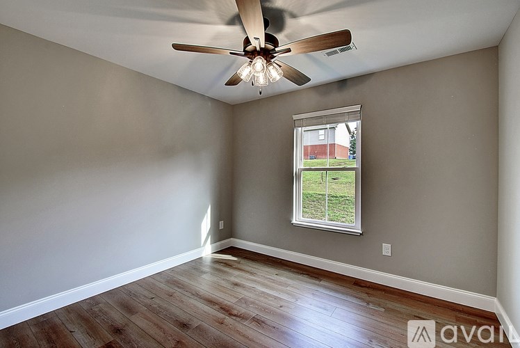 A room with a ceiling fan and a window showing a view of a house.