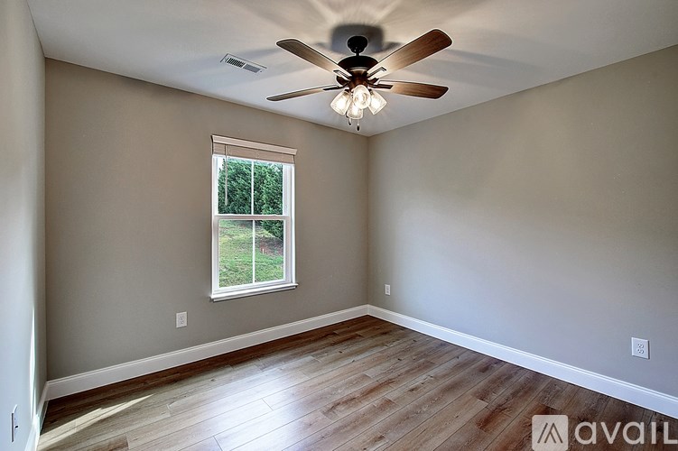 A room with a ceiling fan and a window overlooking a green lawn.