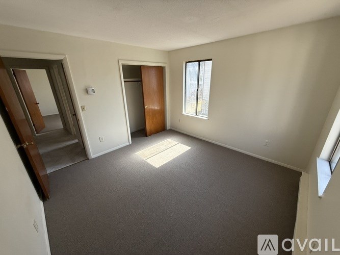 A spacious room with a carpeted floor, a window, and a door leading to another room.