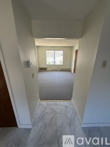 A hallway with a marble floor and white walls leading to a window.
