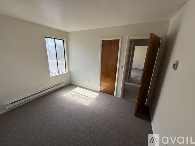 A room with a carpeted floor, a window, a door, and a wall-mounted light switch.