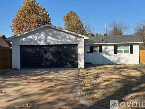 A white house with a black garage door in front of a tree.