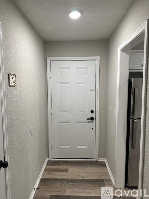 A white door is in a hallway with a refrigerator on the side.