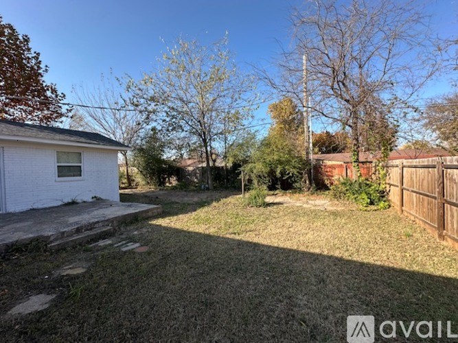 A backyard with a white house, a fence, and trees.