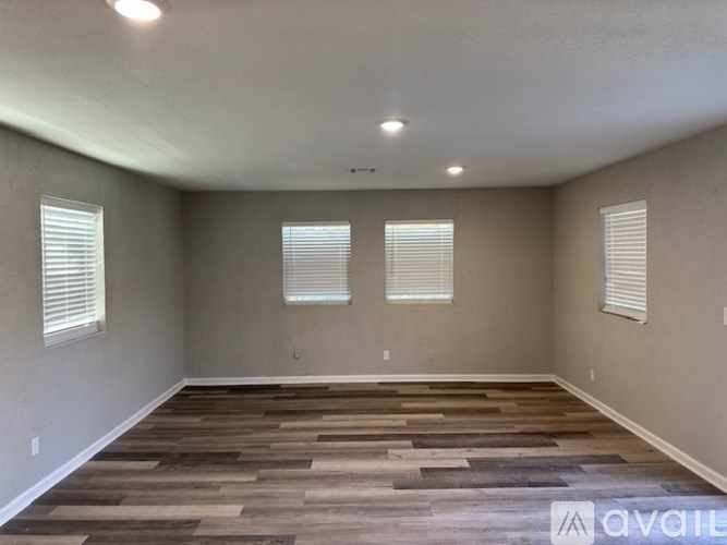 A room with wooden flooring and three windows with blinds.