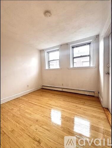 A room with wooden flooring and two windows.