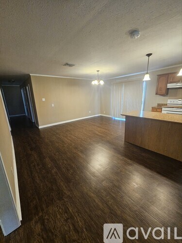 A room with wooden flooring and a kitchen area in the background.