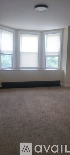 A room with a carpeted floor and three windows.