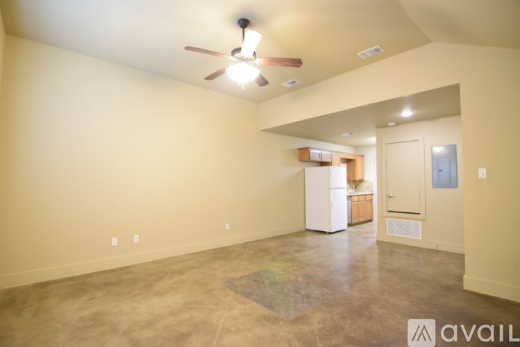 A spacious room with a ceiling fan and a kitchenette in the background.