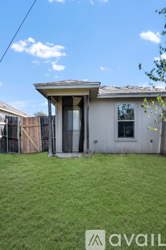 A house with a brown roof and a white door is surrounded by a grassy area.