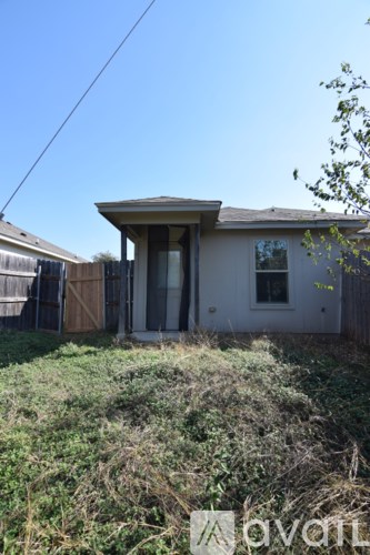A house with a brown roof and a white door is surrounded by a grassy area.