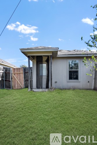 A house with a brown roof and a white door is surrounded by a grassy area.
