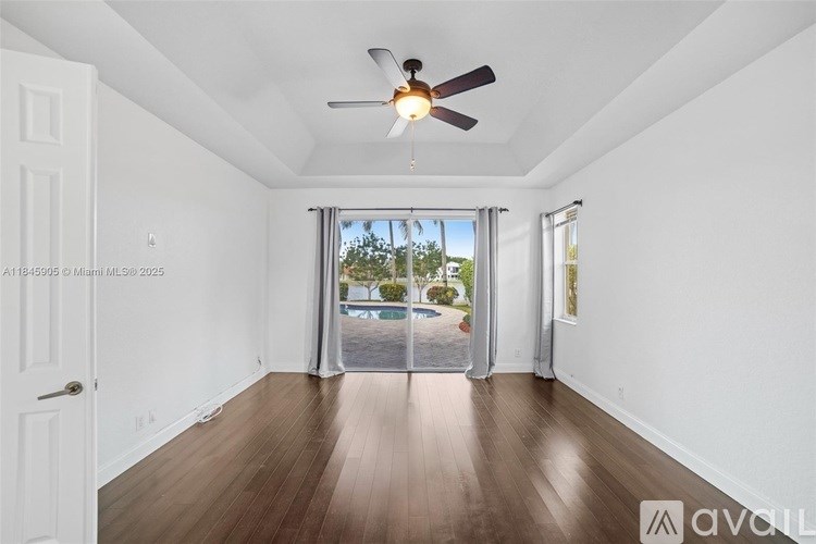 A spacious room with a ceiling fan and sliding glass doors leading to a balcony.