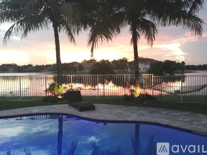 A pool surrounded by palm trees with a sunset in the background.