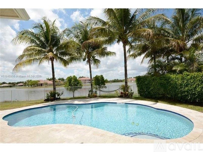 A pool surrounded by palm trees and a white fence.