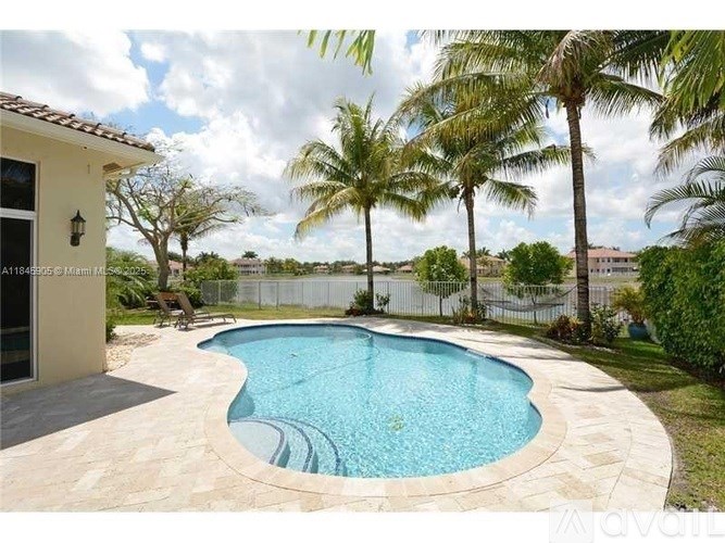 A pool surrounded by palm trees and a white fence.