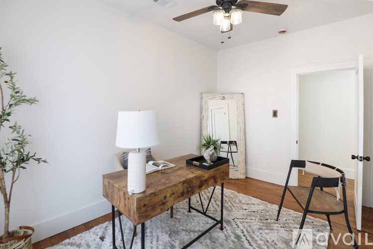 A room with a wooden table, a white lamp, a plant, and a chair.