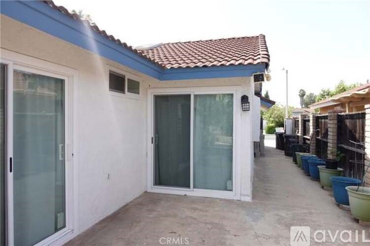 A house with a blue roof and white walls has a patio with a glass door.