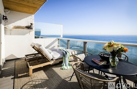 A balcony with a table, chairs, and a view of the ocean.