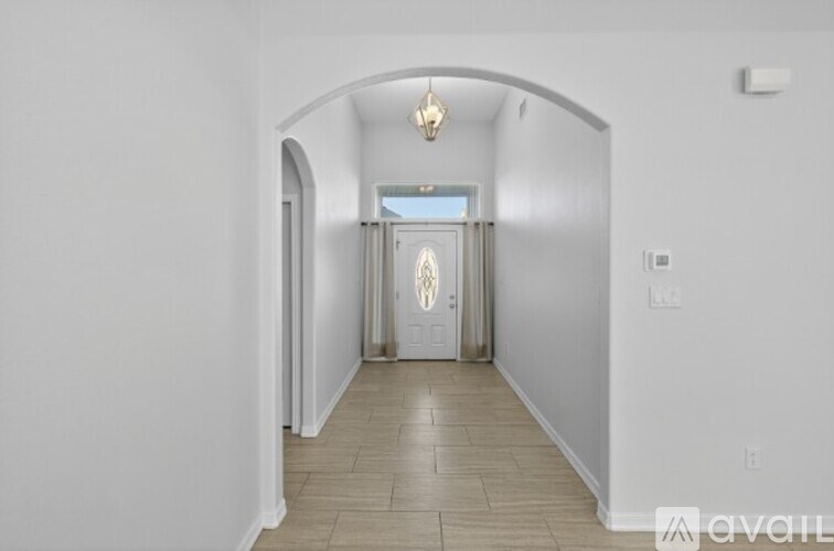 A hallway with a door at the end and a light fixture hanging from the ceiling.