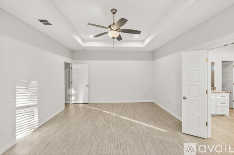A spacious room with a ceiling fan and light, hardwood floors, and white walls.