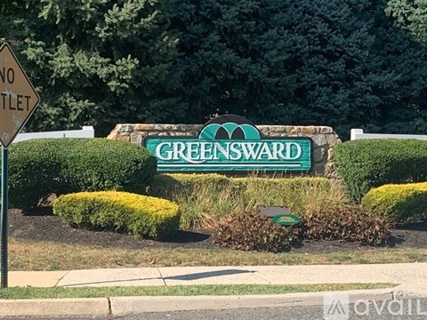 A sign that says Greensward is in front of a hedge.
