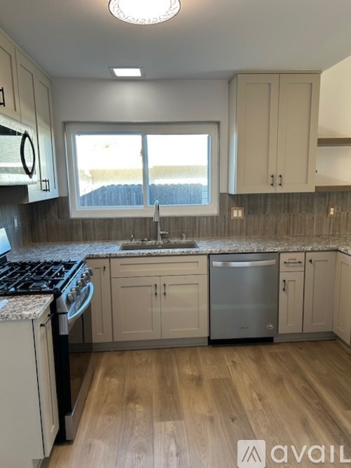 A kitchen with wooden floors and a window overlooking a fence.