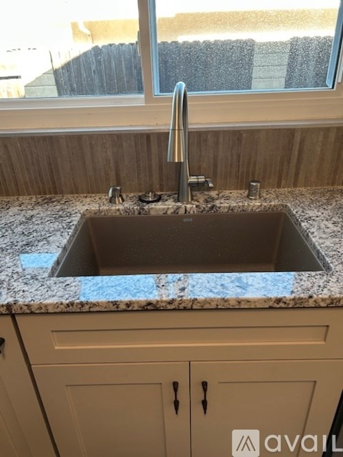 A kitchen sink with granite countertop and wooden cabinets.