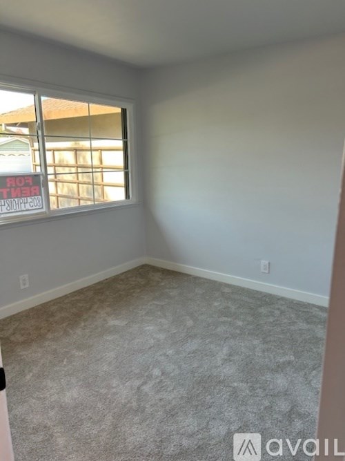 A room with a carpeted floor and a window showing a sign that says "For Rent".