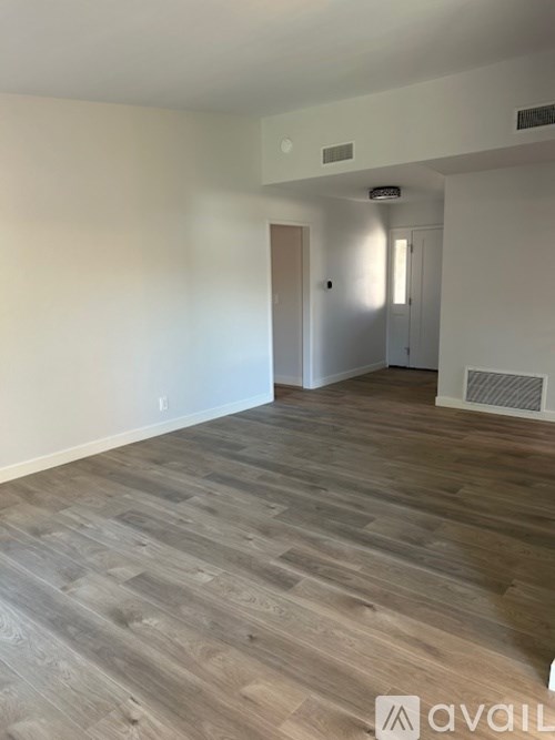 A room with wooden flooring and a door on the left.