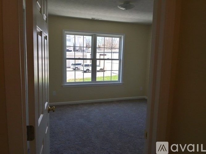 A room with a carpeted floor and a window overlooking a parking lot.
