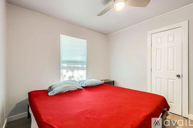 A bedroom with a red bedspread and a window.