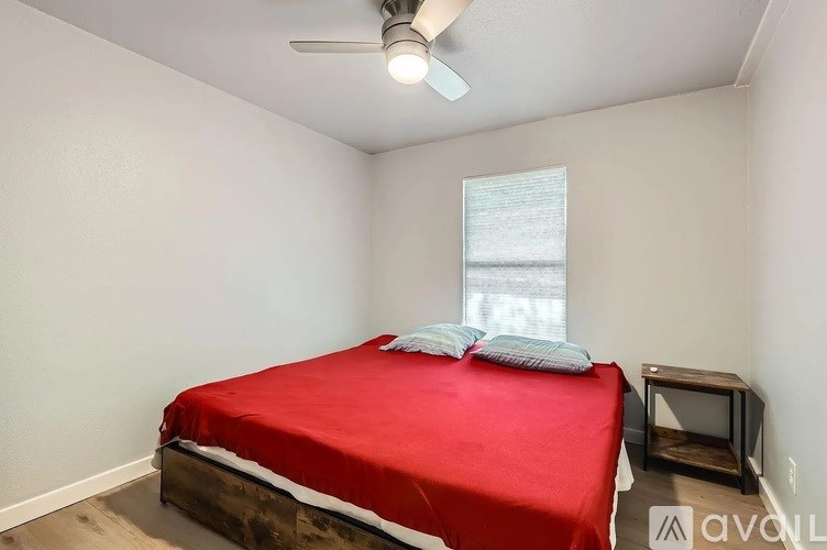 A bedroom with a red bedspread and a ceiling fan.