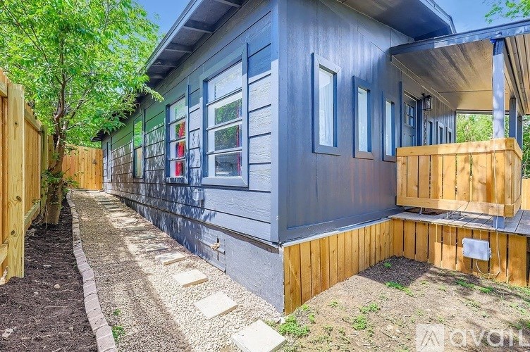 A blue house with a wooden deck and a gravel pathway.