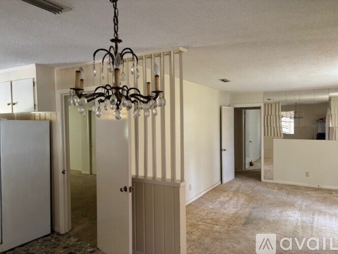 A chandelier hangs in a well-lit room with a kitchen visible in the background.