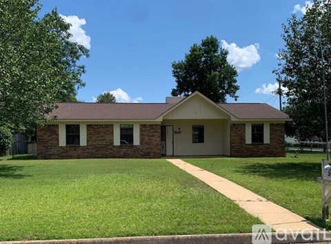A house with a brown roof and a white door is surrounded by a green lawn.