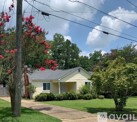 A house with a lawn and a tree with red flowers in front.