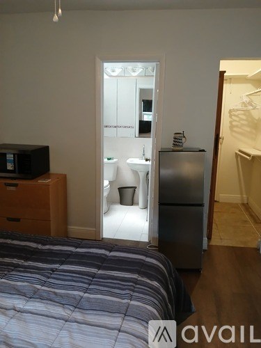 A bedroom with a bed, a dresser, and a fridge.