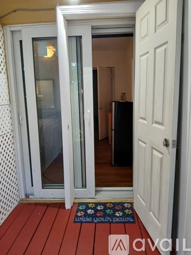 A white door with a glass panel is open to a room with a black refrigerator.