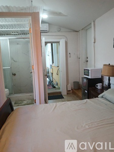 A bedroom with a bed, a desk with a lamp, and a bathroom with a glass shower door.